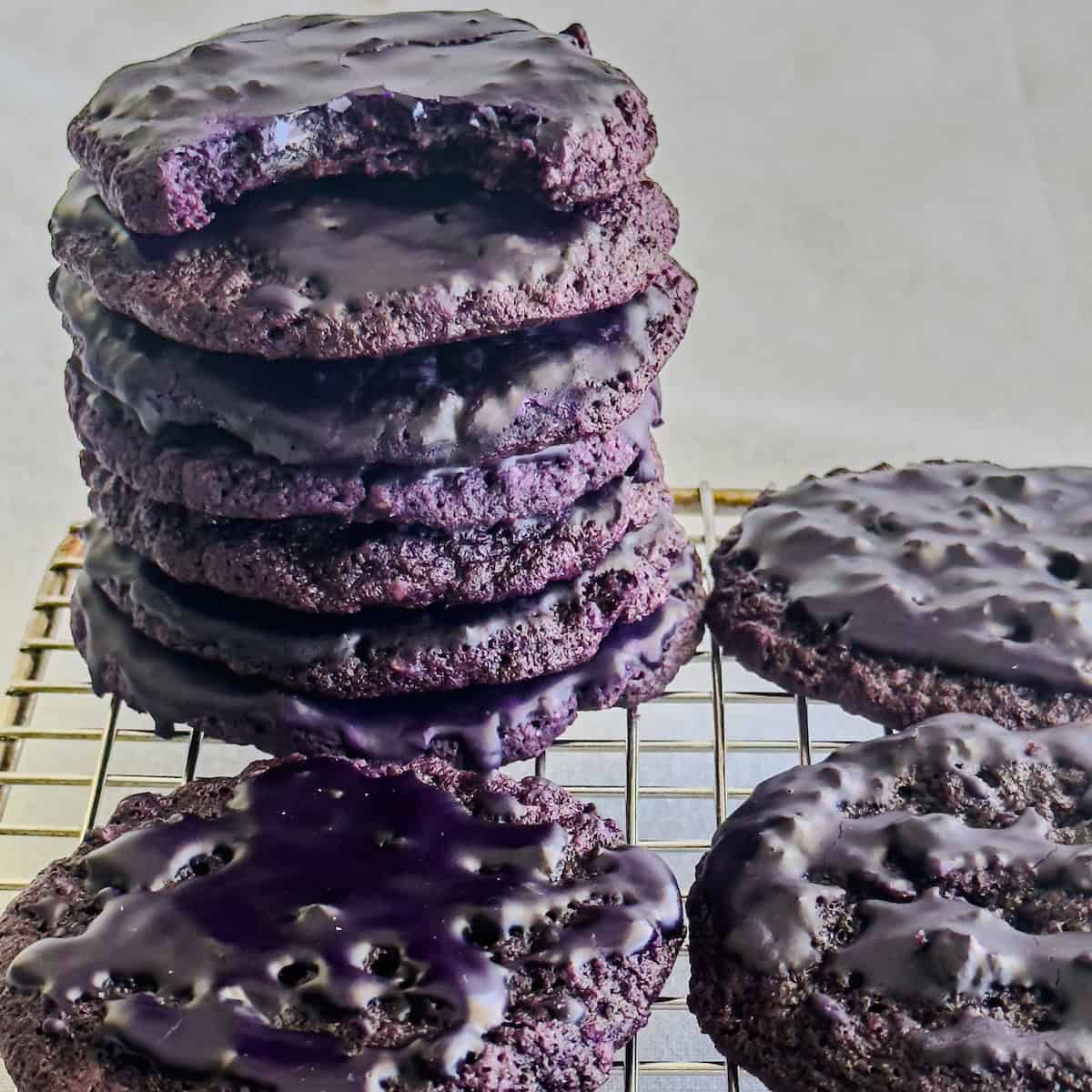 Iced ube oatmeal cookies piled on a cooling rack