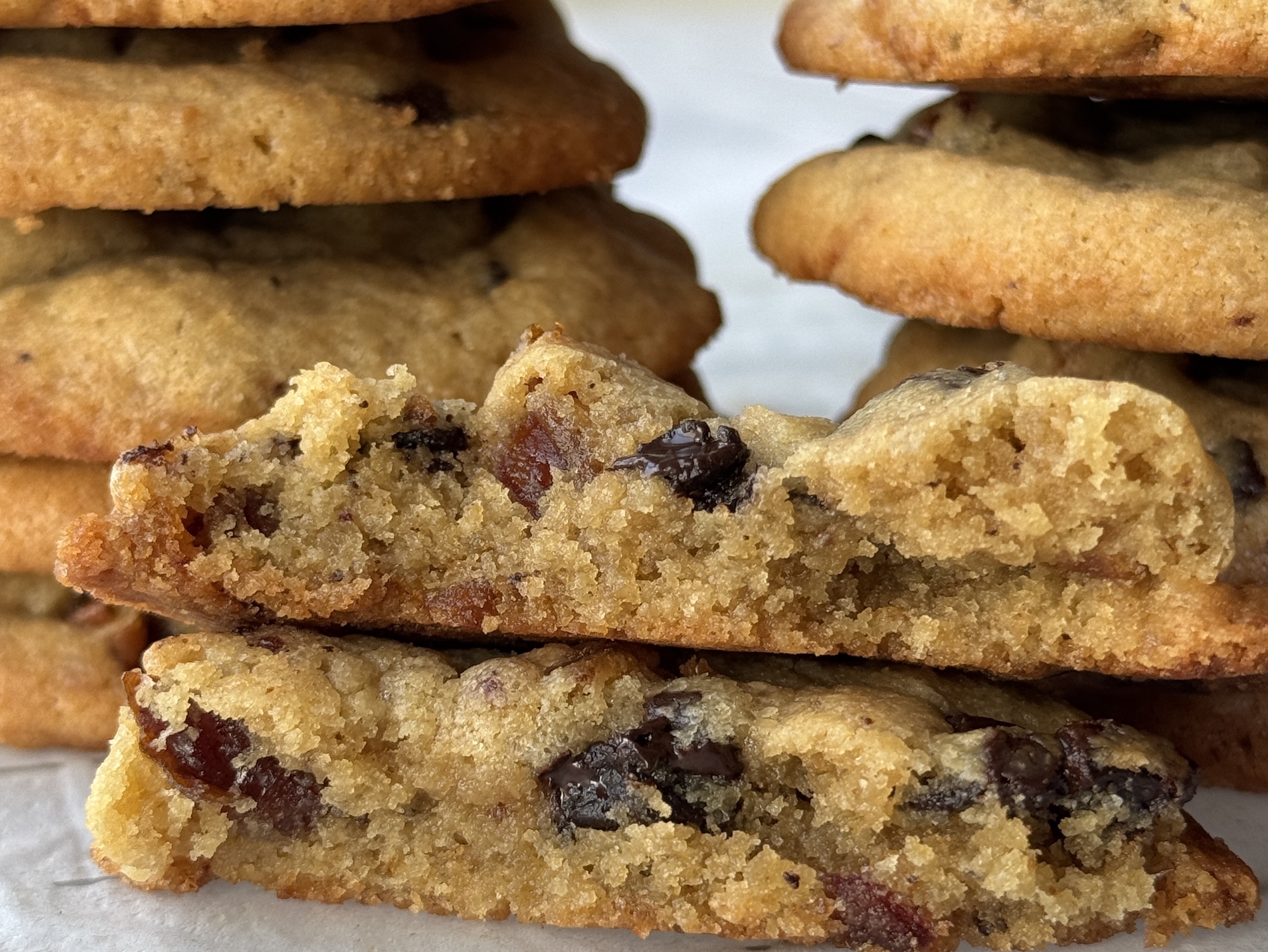 Baked cookies piled in two columns behind a cookie broken in half to show dates and chocolate inside