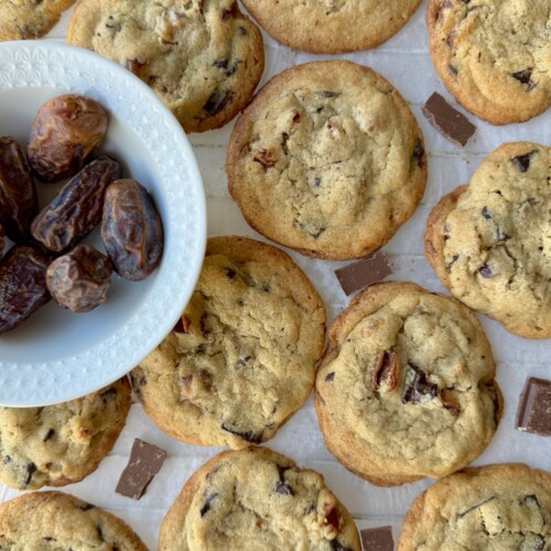 Tahini Date Chocolate Chunk Cookies in a single layer with chocolate pieces in between and a bowl of dates to the side