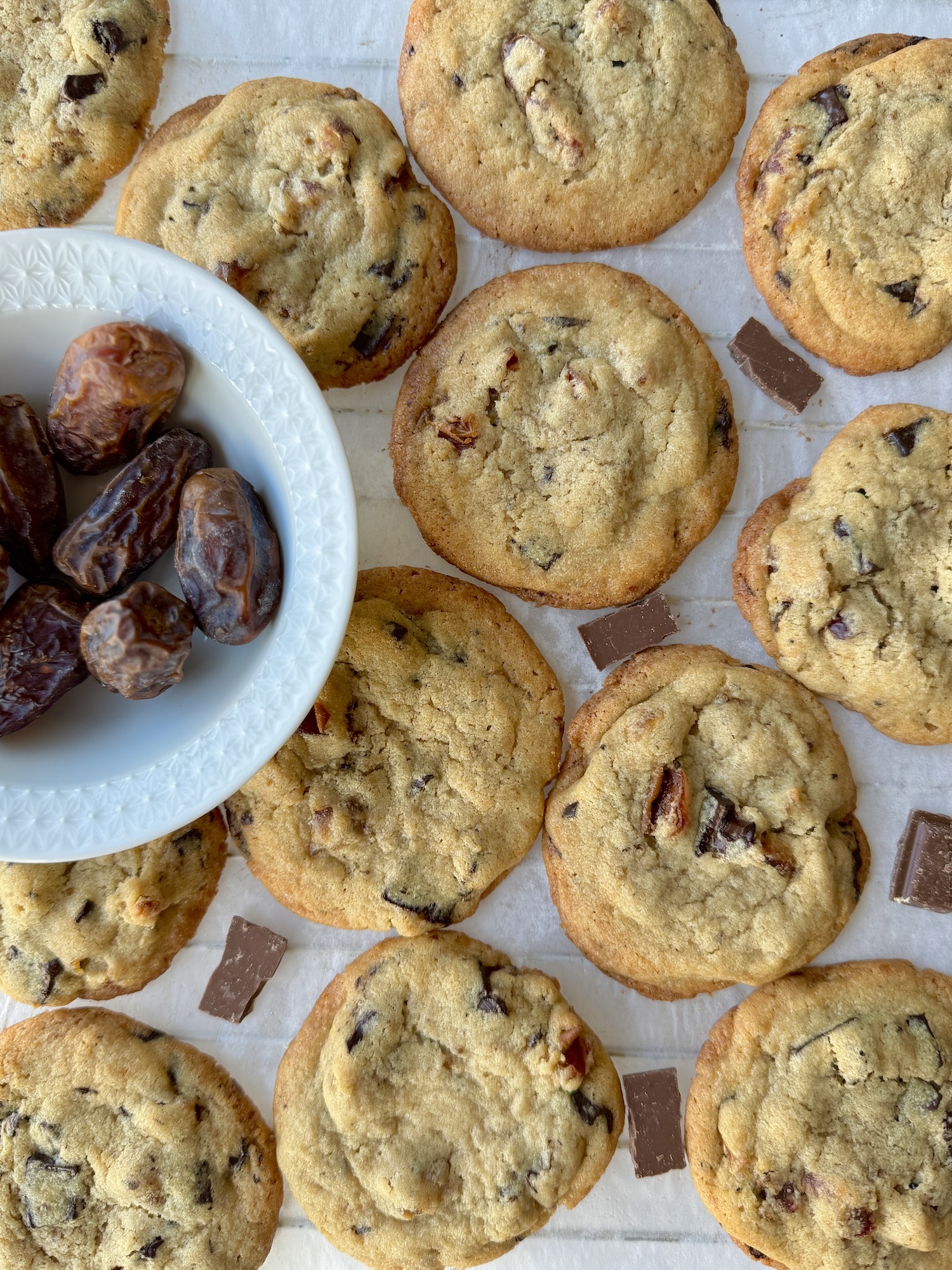 Tahini Date Chocolate Chunk Cookies in a single layer with chocolate pieces in between and a bowl of dates to the side