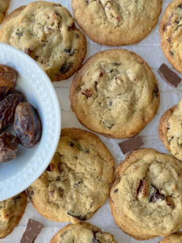 Tahini Date Chocolate Chunk Cookies in a single layer with chocolate pieces in between and a bowl of dates to the side