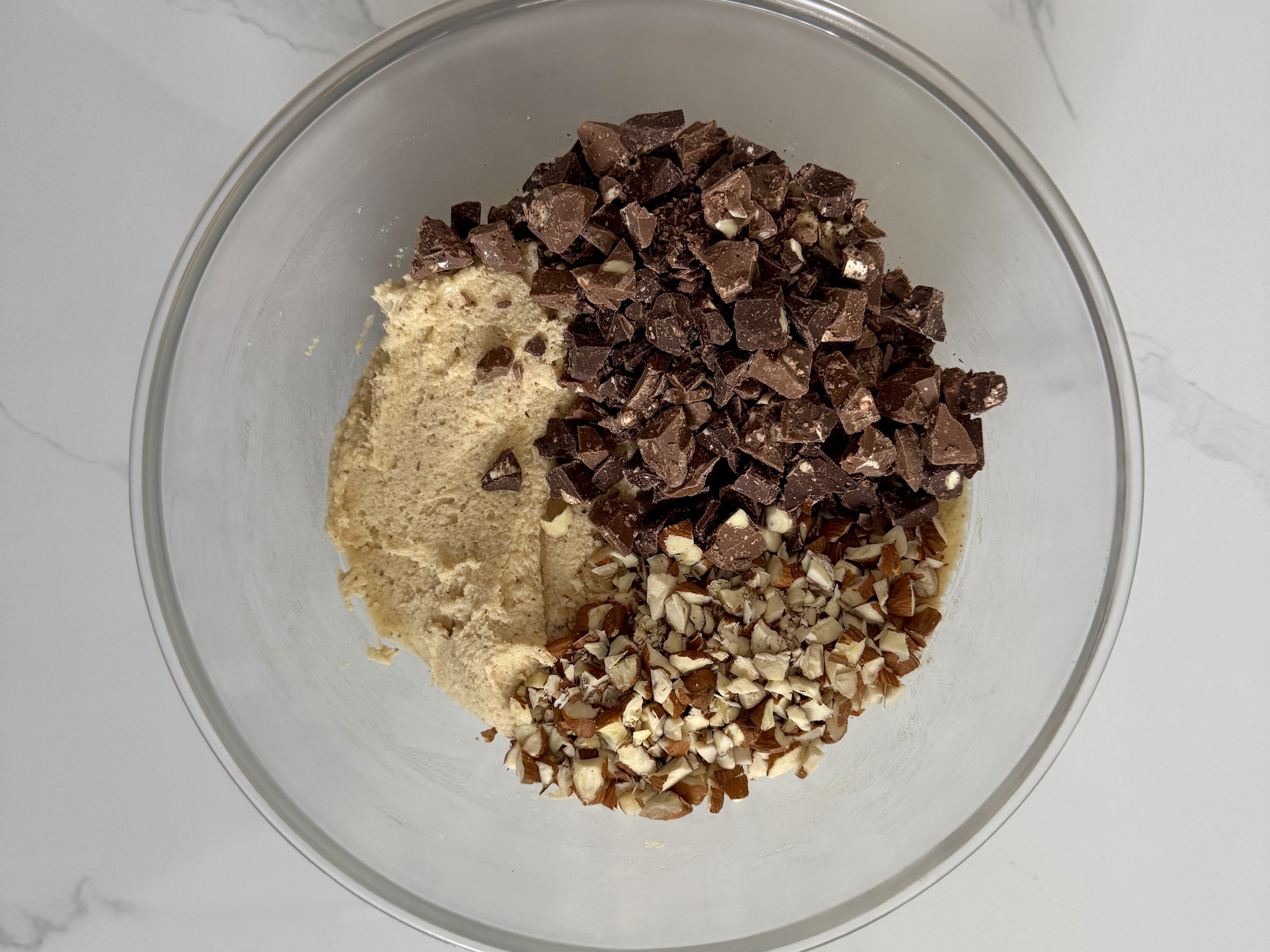 Chopped almonds and Toblerone ready to mix into dough in glass bowl