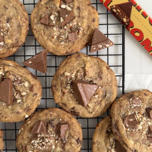 Brown Butter Almond Honey Toblerone Cookies on a cooling rack with a Toblerone package