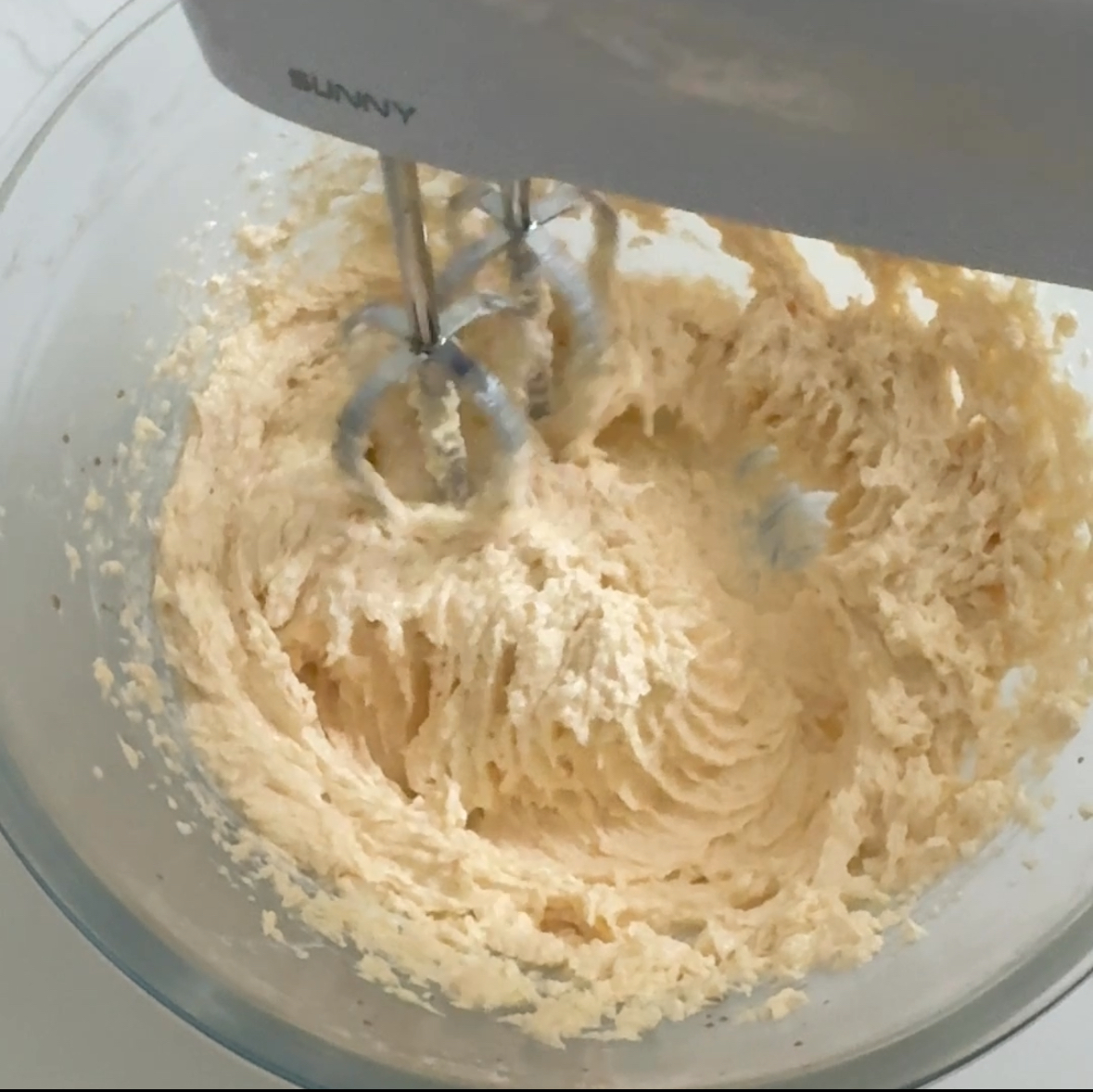 Wet ingredients of dough mixed in glass bowl with hand mixer
