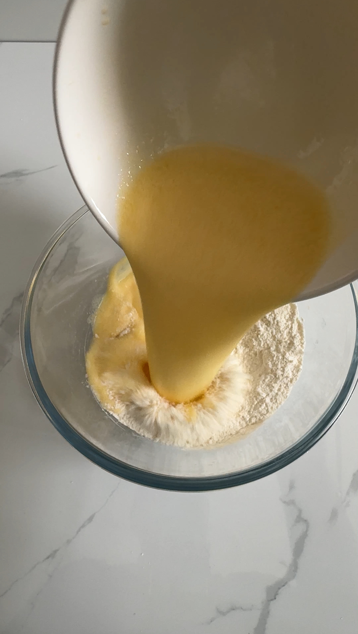 Wet ingredients added to dry ingredients in a glass bowl