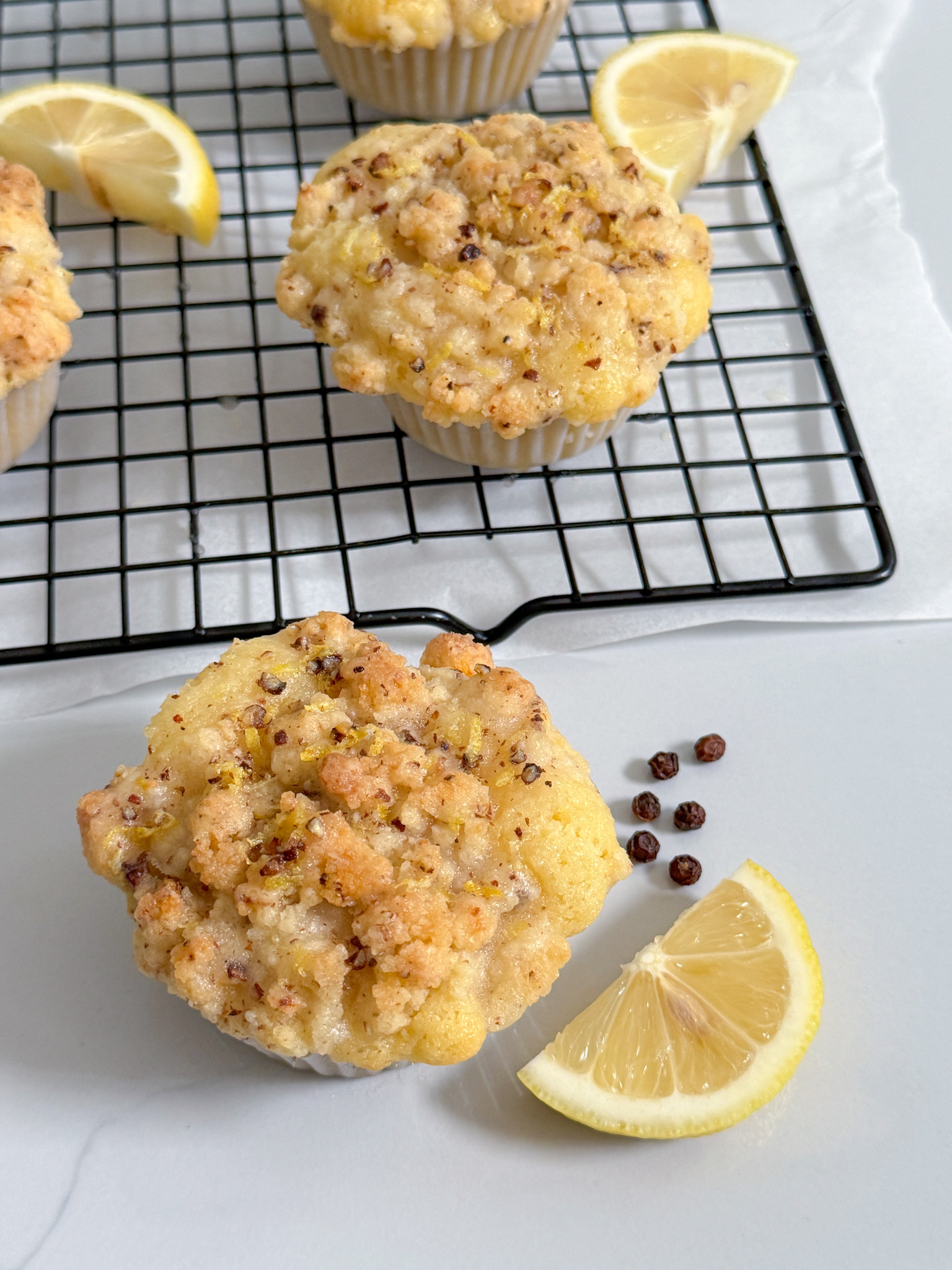 Glazed lemon muffins with streusel on cooling rack with lemon slice and peppercorn